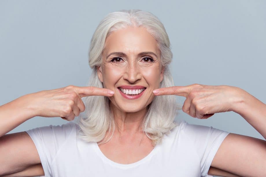 smiling woman points to her dental implants